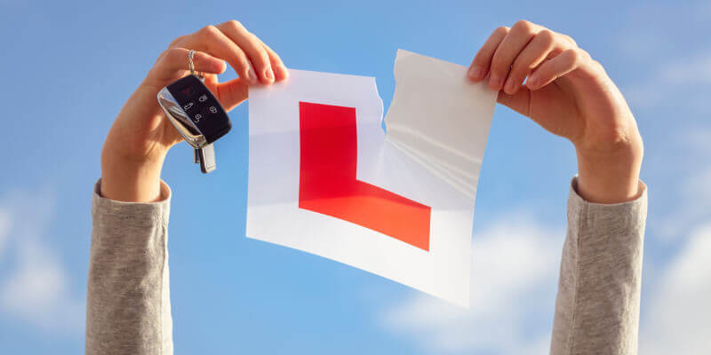 Hands holding car keys and ripping an l-plate in half