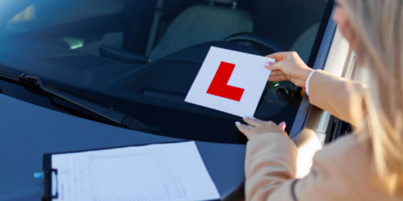 Woman placing l-plate onto car windscreen