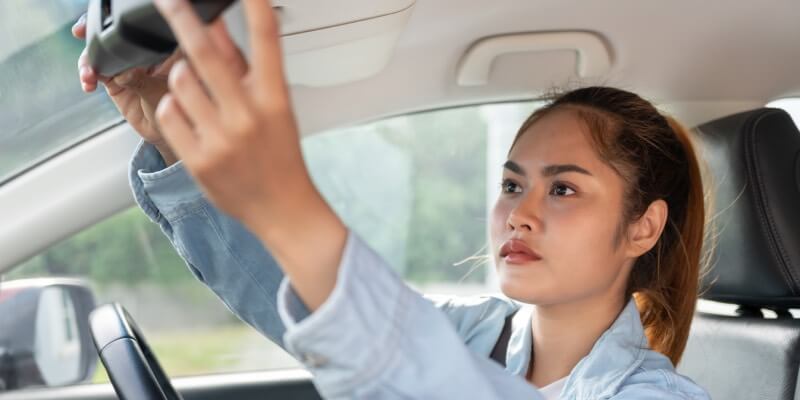 Girl reaching to adjust the rearview mirror in car
